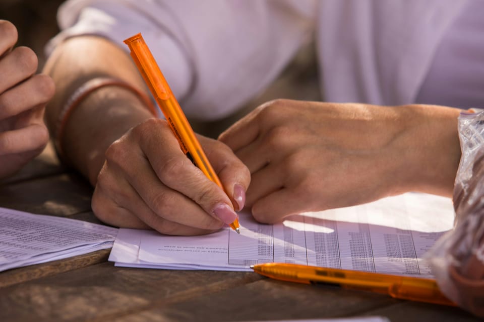 Image: Close up of a pair of hands holding an orange pen looking at a printed spreadsheet.